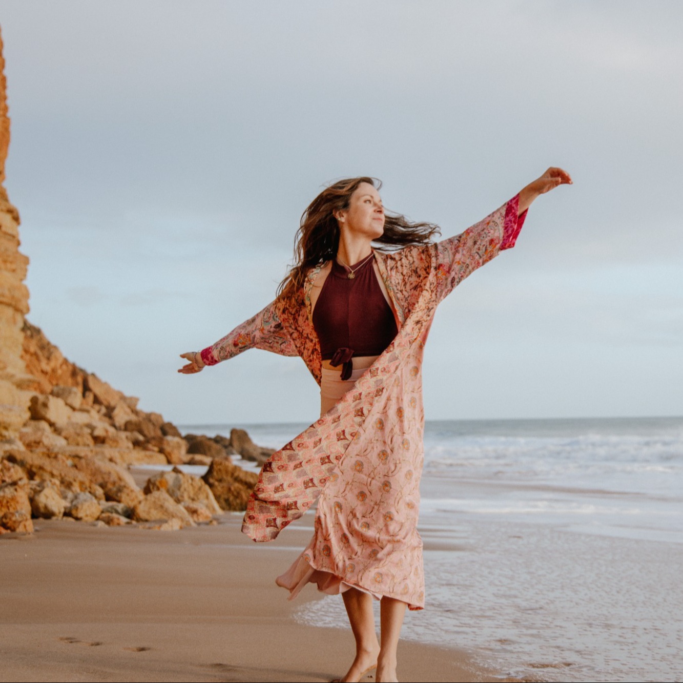 Élise Pieters sur une plage, bras ouverts, kimono rose au vent